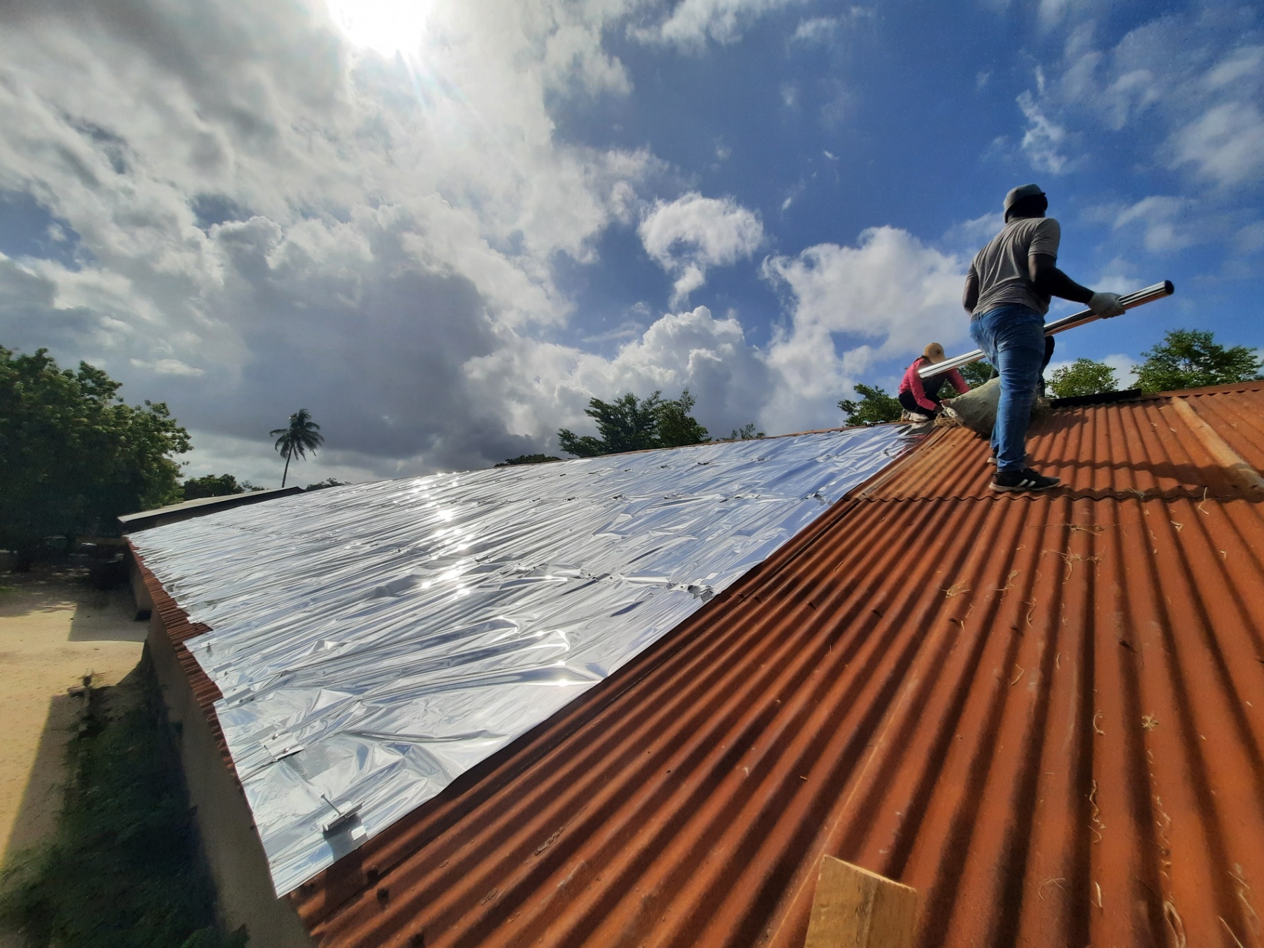 Reflective sheeting spanning the length of a classroom block under a Dar es Salaam sky.