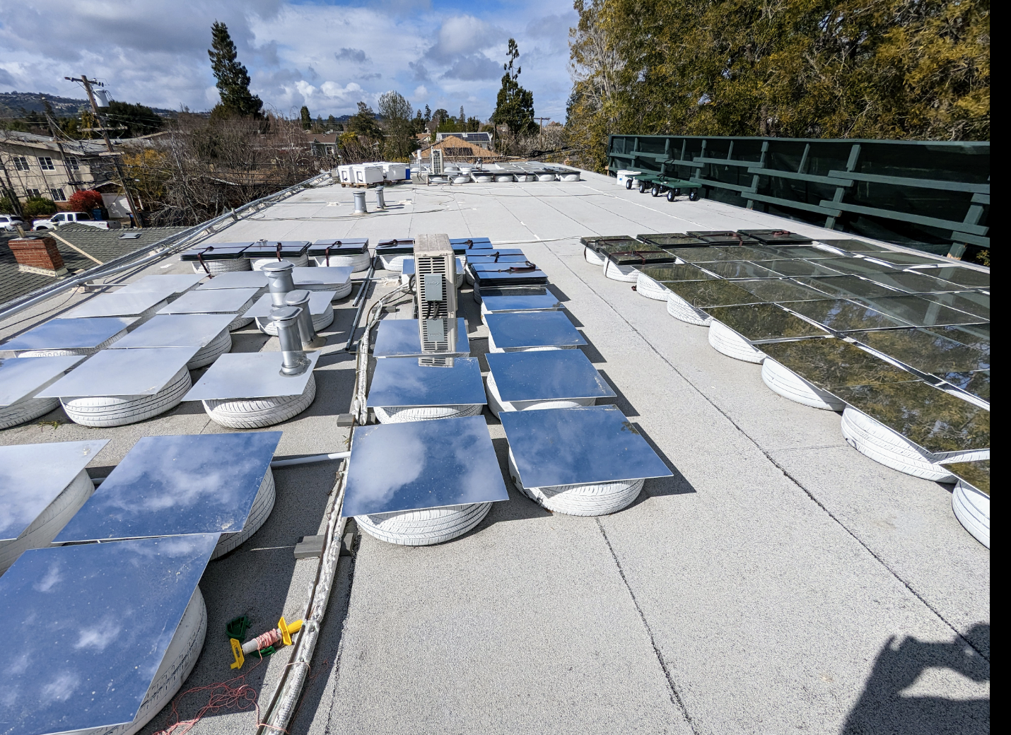 Wide view of the California rooftop testbed — glass-mirror panels arranged across tire supports alongside instrumentation and weather sensors.