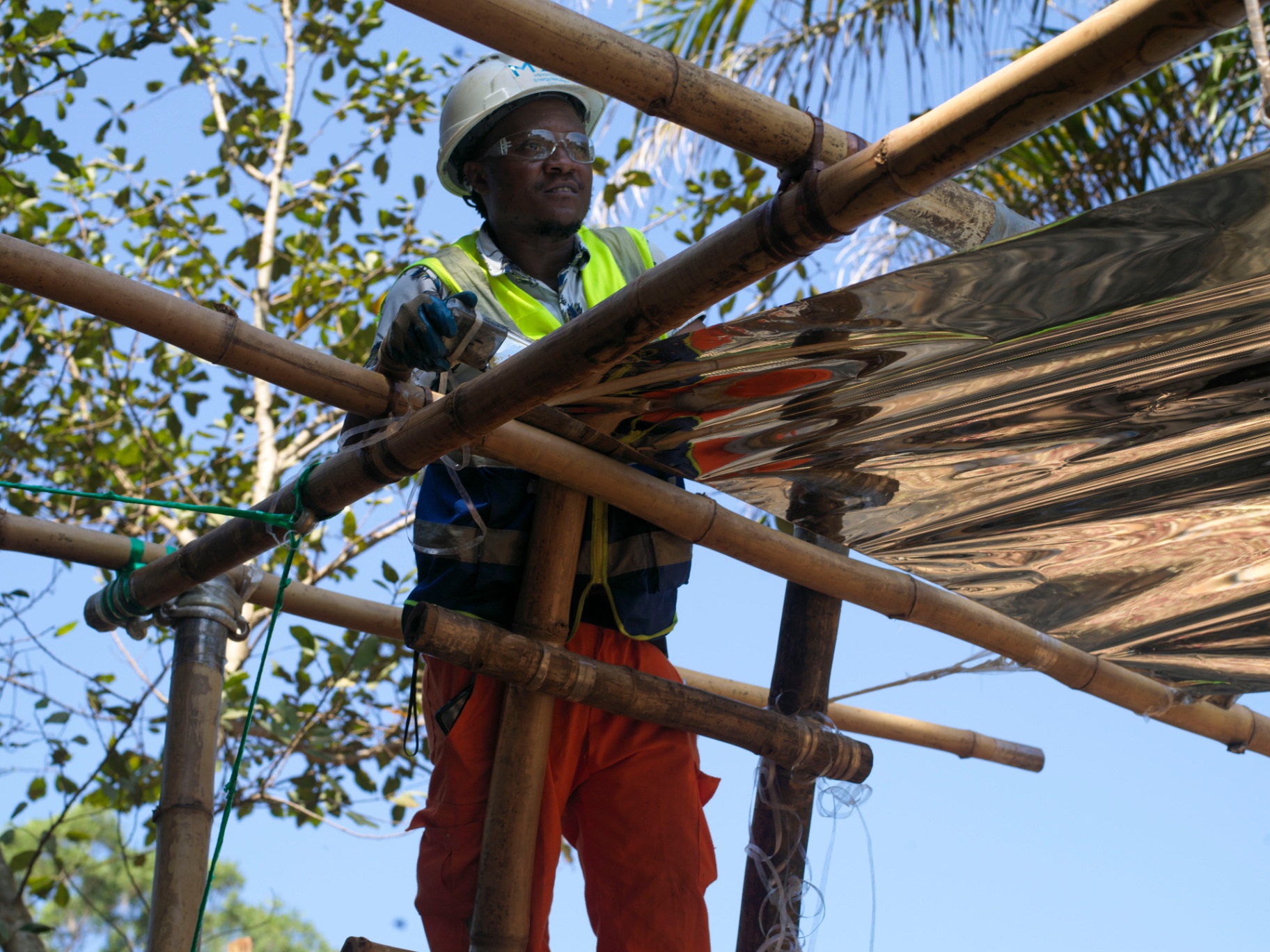 Installer fitting reflective sheeting to a bamboo canopy