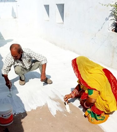 Dos personas aplicando un recubrimiento blanco reflectante en un tejado.