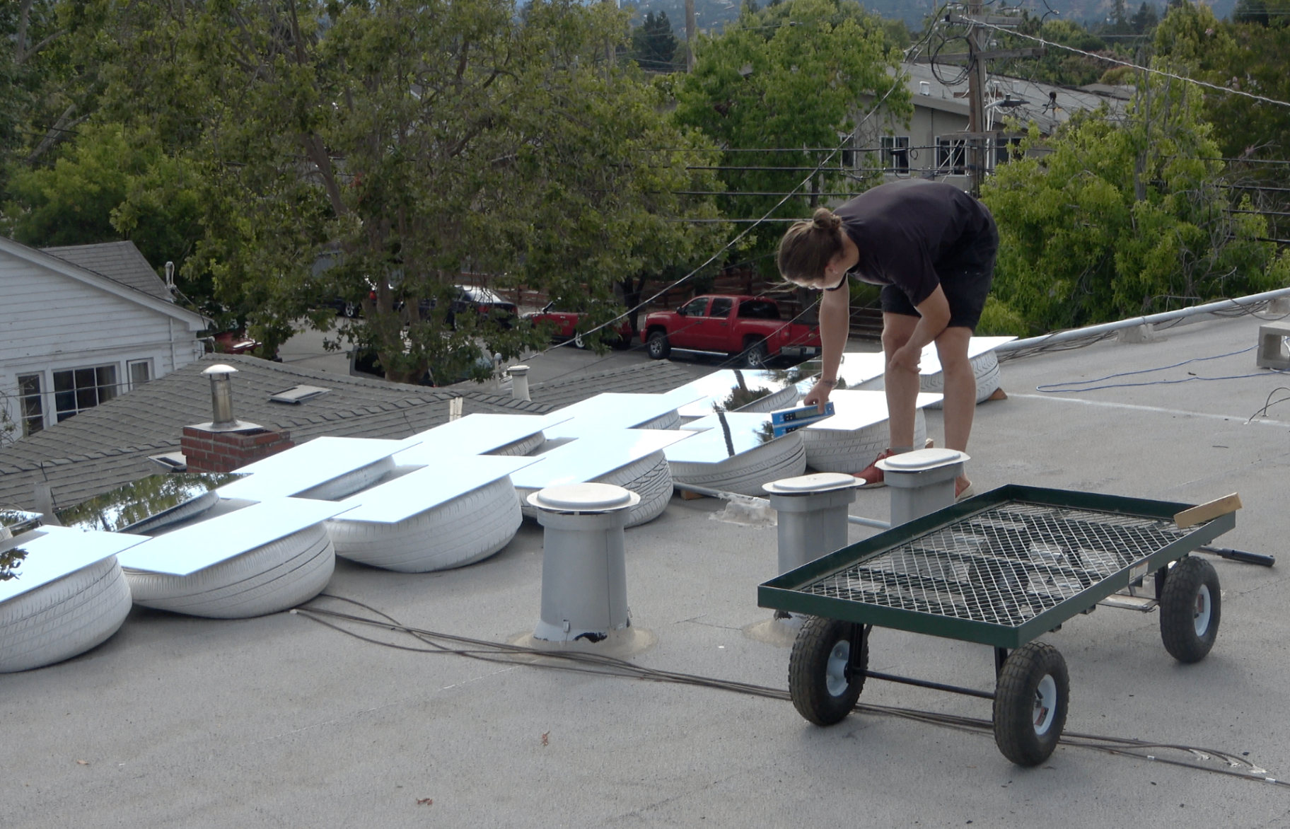 A researcher levelling reflective panels across the rooftop array, ensuring consistent geometry for comparative temperature measurements.