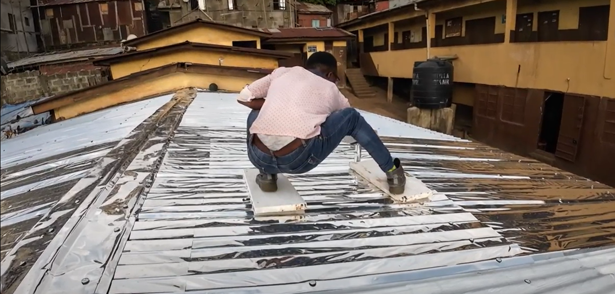 MEER installer fitting reflective sheeting across a rooftop at the FAWE site in Freetown
