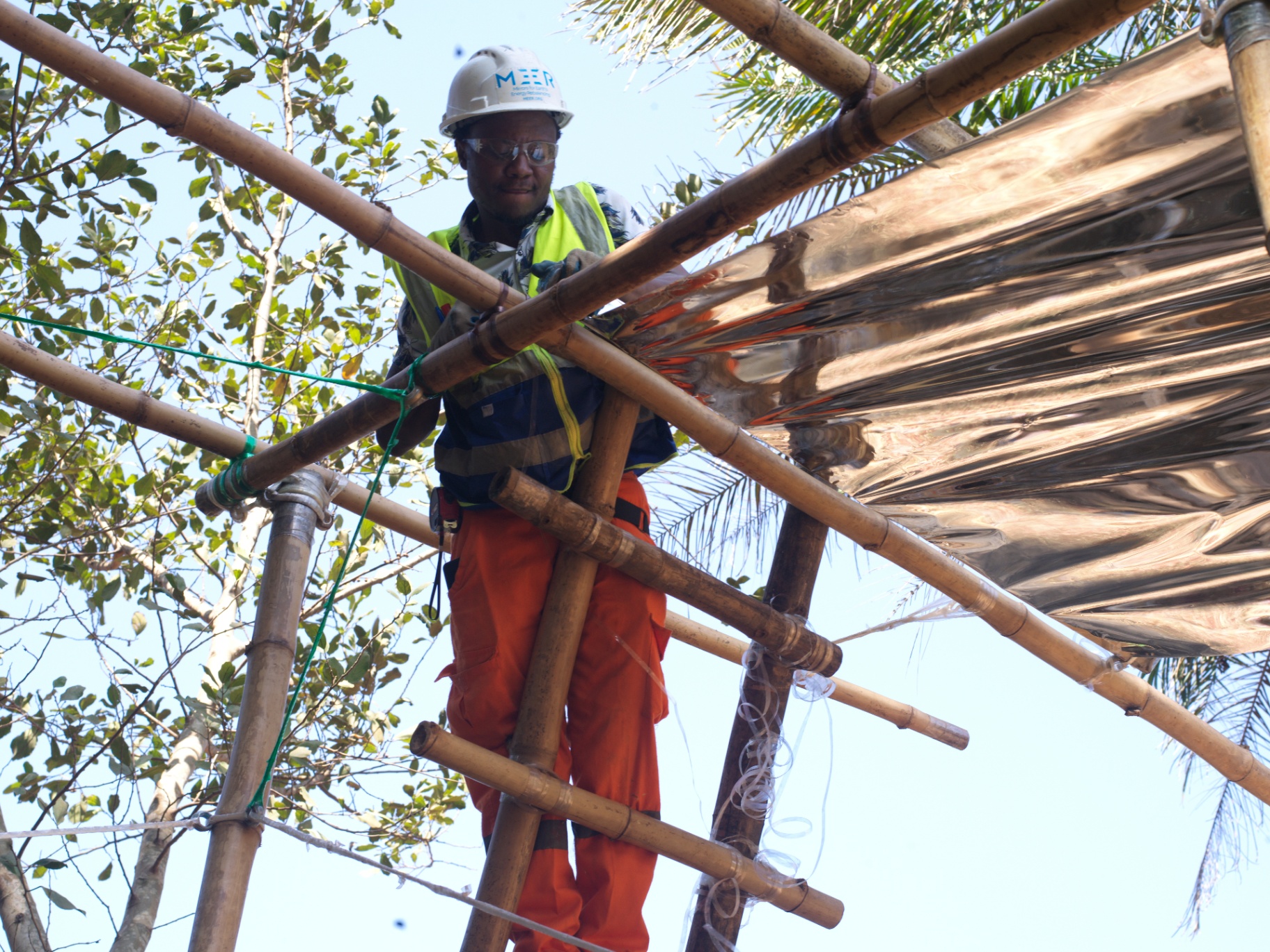 Installer fitting reflective sheeting on a bamboo canopy frame